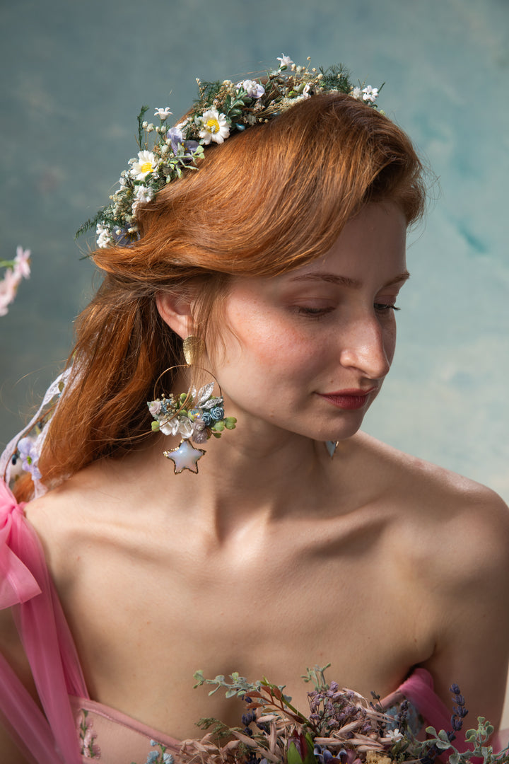 Woman with floral headpiece and earrings against a soft blue background