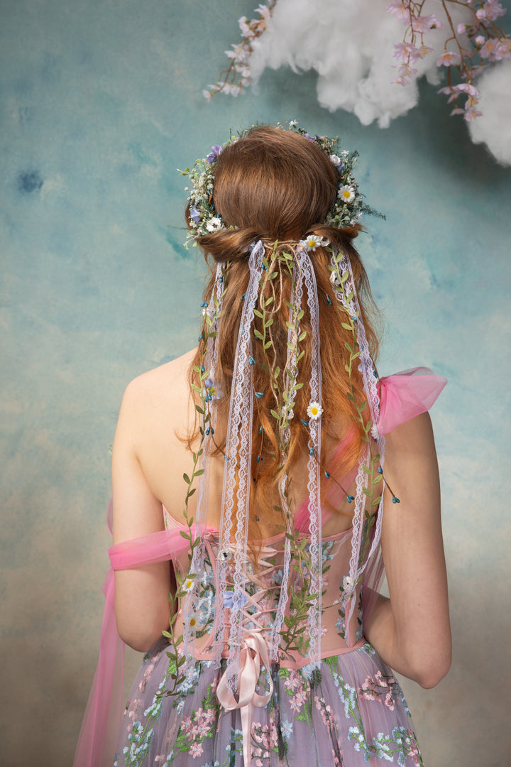 Person with floral hair accessories and a fairy costume against a soft, multicolored background