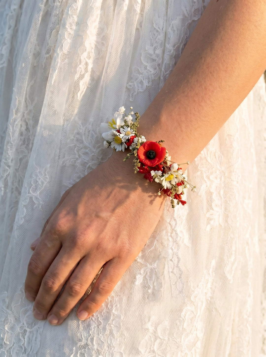 Hand wearing a floral bracelet with red flowers on a white lace fabric background