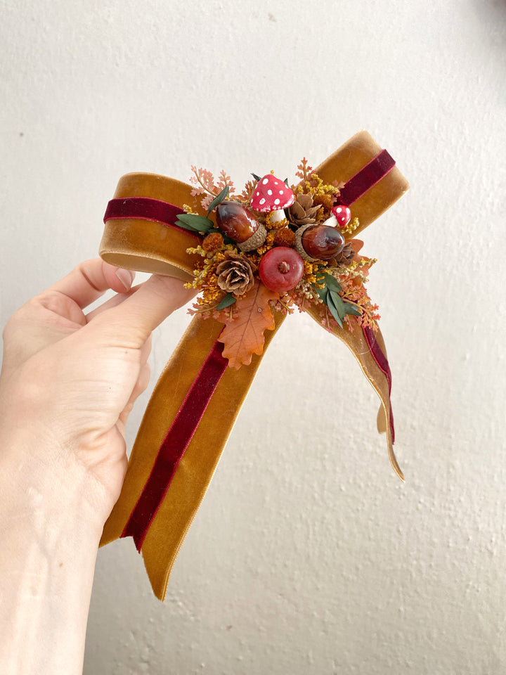 A hand holding a  handmade red and white toadstool brings a playful touch to layered ribbons and warm botanical textures