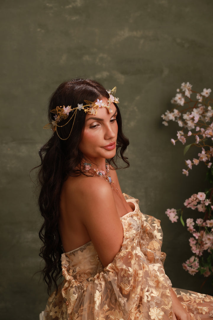 Woman in a floral dress with a flower crown against a dark green background with cherry blossoms.