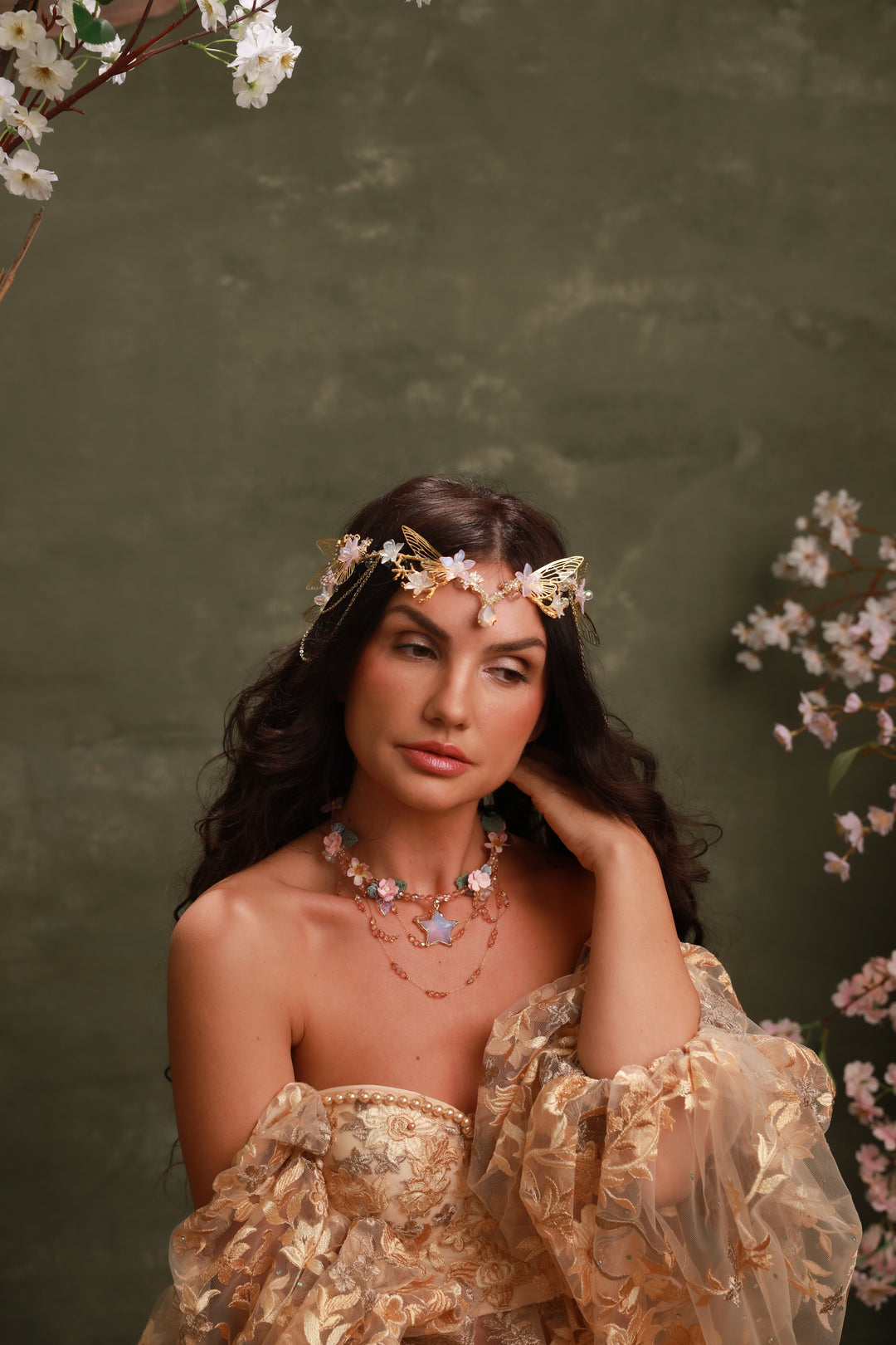 Woman wearing a floral headpiece and jewelry against a green background with flowers.