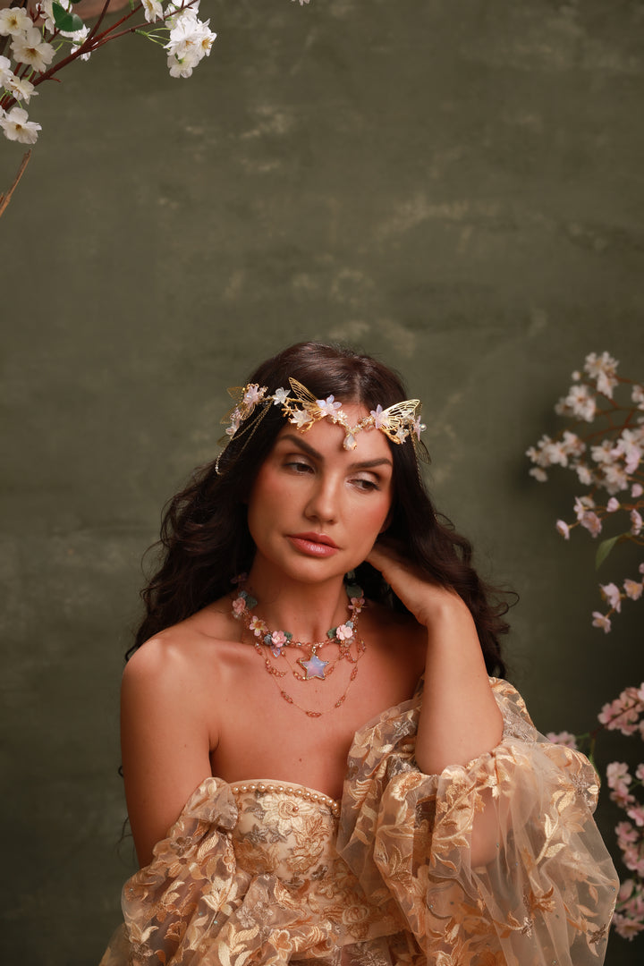 Woman wearing a floral headpiece and jewelry against a green background with flowers.