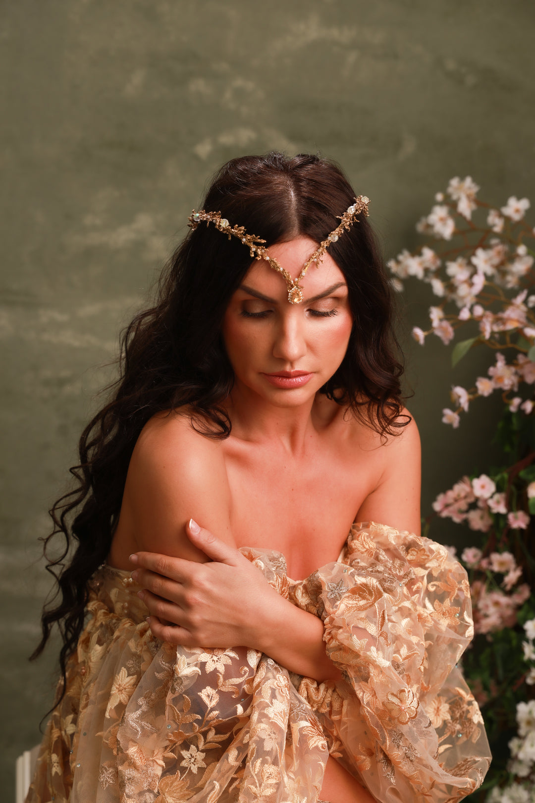 Woman in a gold dress with floral headpiece against a green background with flowers