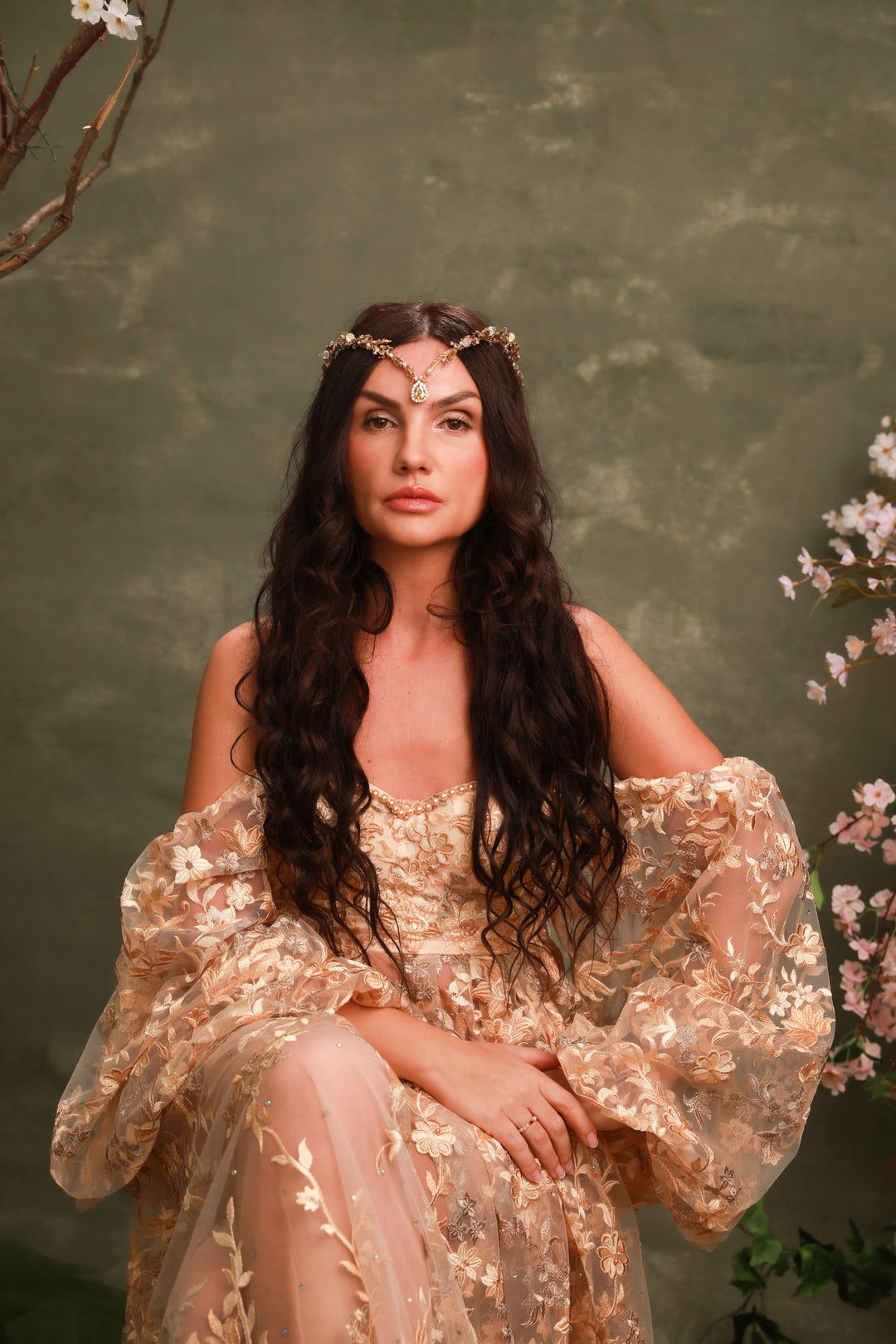 Woman in a gold dress with floral headpiece against a green background