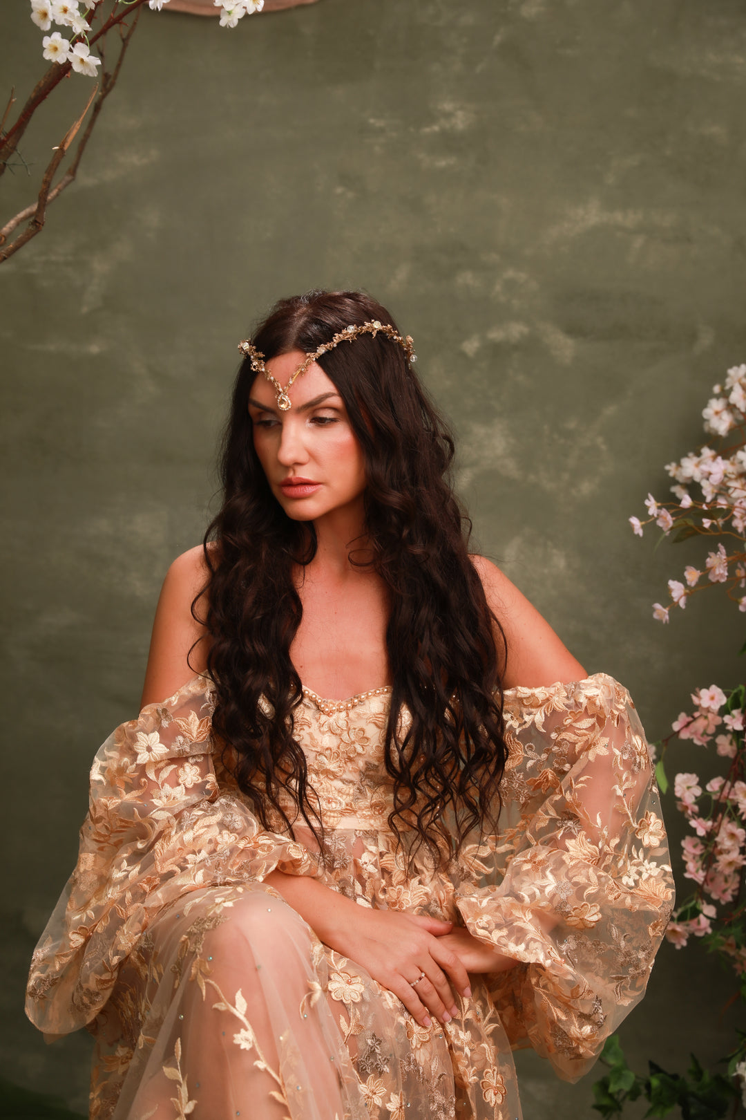 Woman in a gold dress with golden  floral headpiece with crystals  against a green background