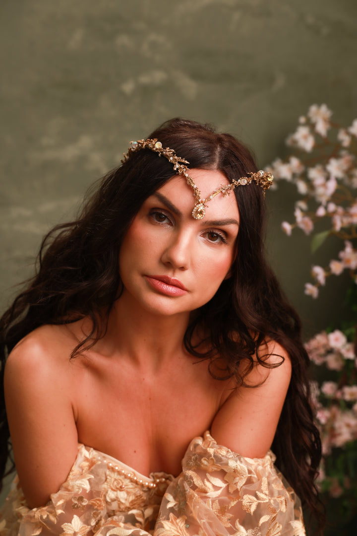 Woman wearing a gold headband with flowers against a green background