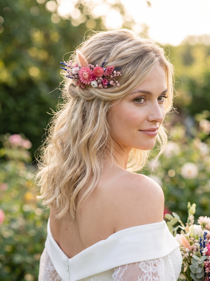 A blonde bride wearing a bohemian-style floral hair accessory with a small pink dried hair comb photographed outdoors in a garden setting.