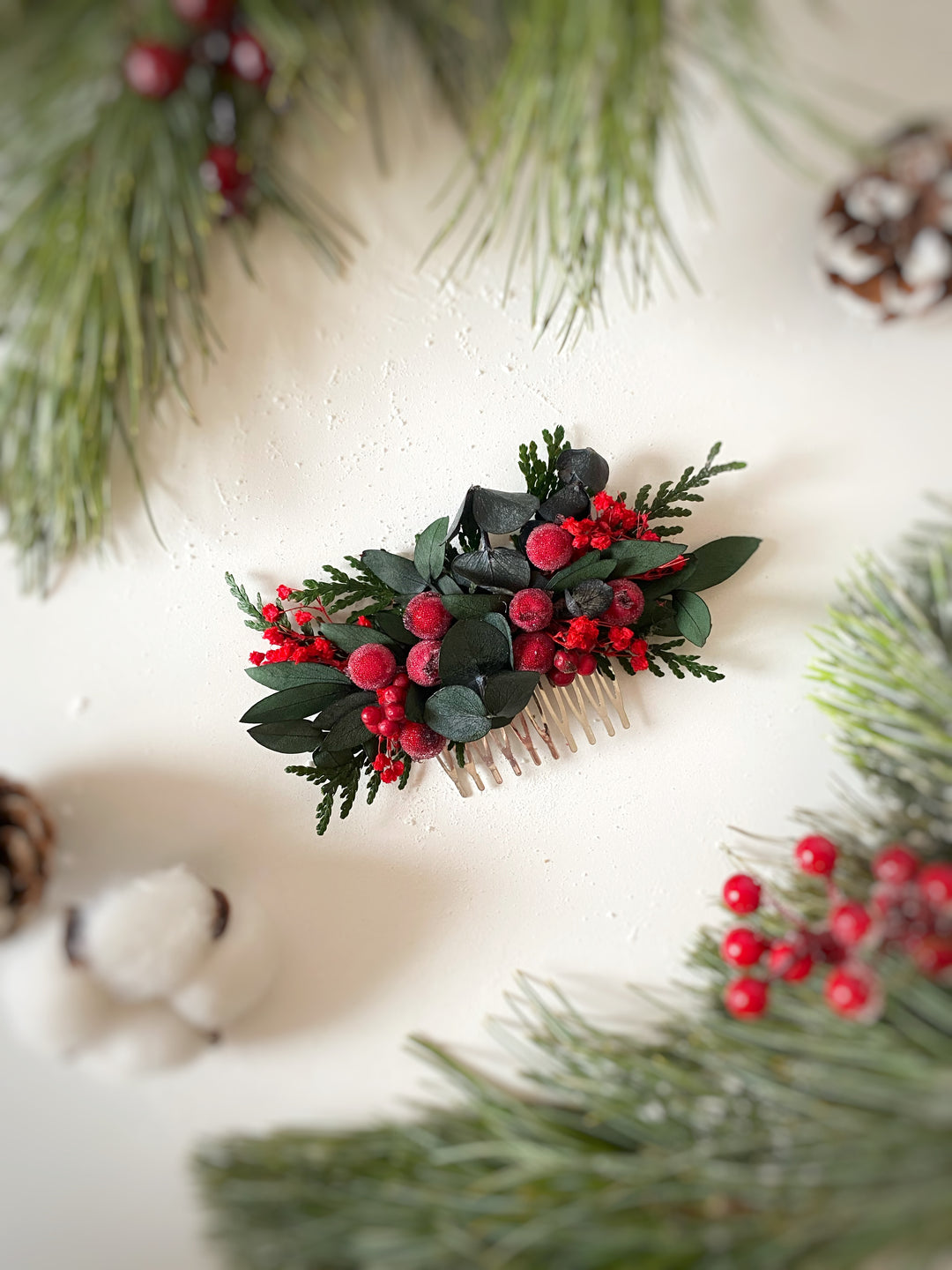 A small Christmas-themed hair comb featuring green eucalyptus leaves, pine branches, red berries, styled on a white background with festive pine branches and cotton bolls.