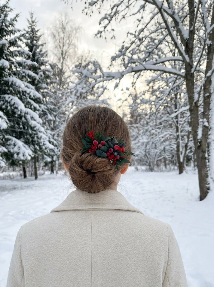 A woman viewed from behind in a snowy outdoor setting, wearing a cream-colored coat and a brown hair accessory with red berries and green leaves.