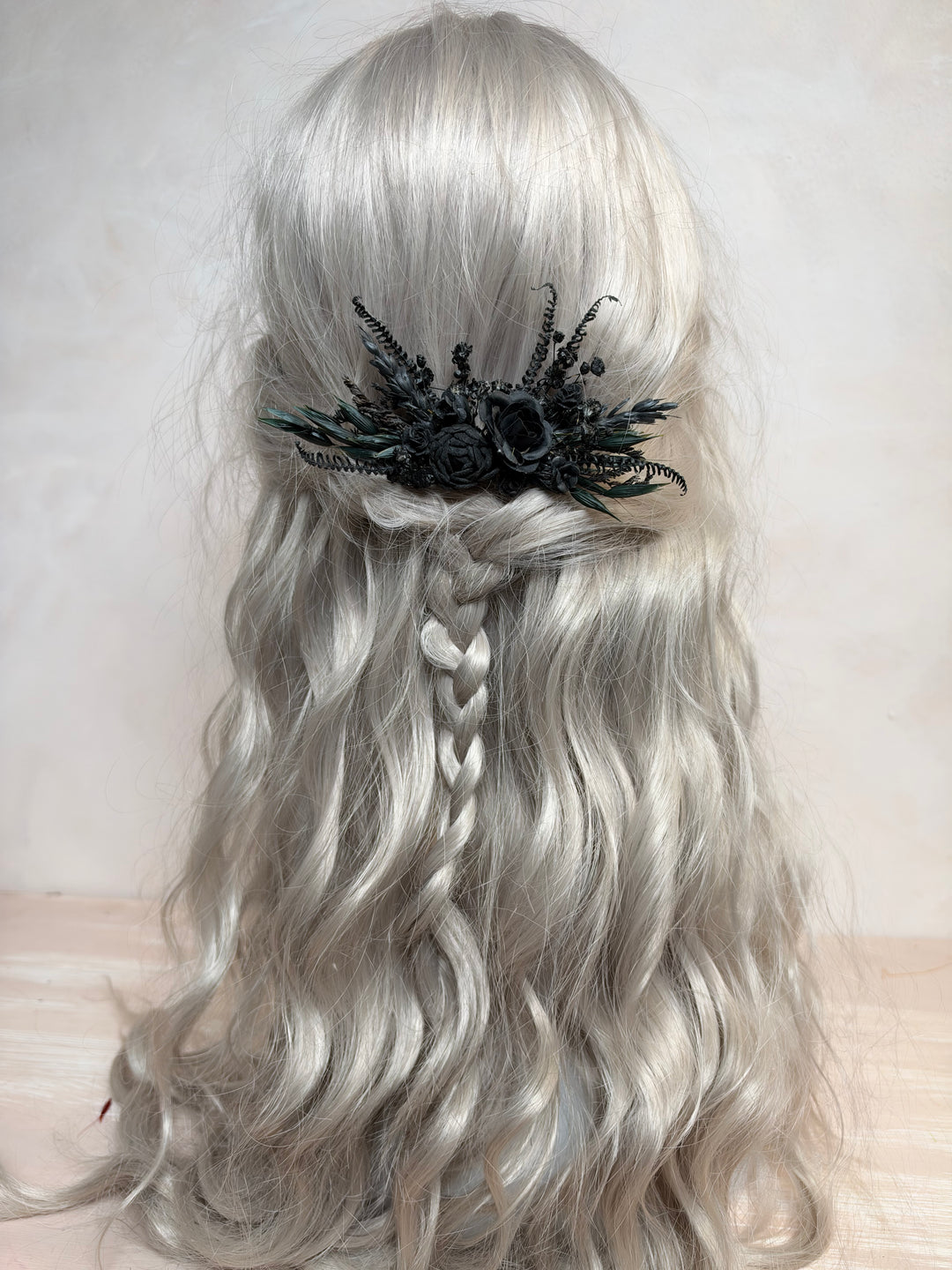 Long wavy silver-gray wig with a half-up style, braided center section, and a black floral hair accessory, shown against a plain light background.