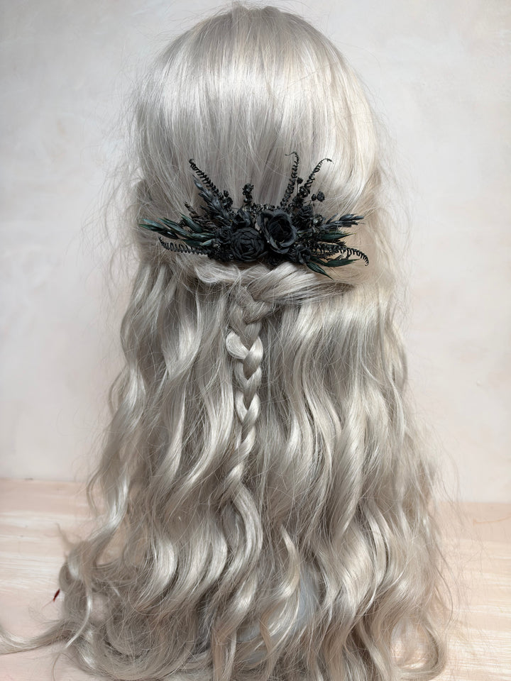 Long wavy silver-gray wig with a half-up style, braided center section, and a black floral hair accessory, shown against a plain light background.