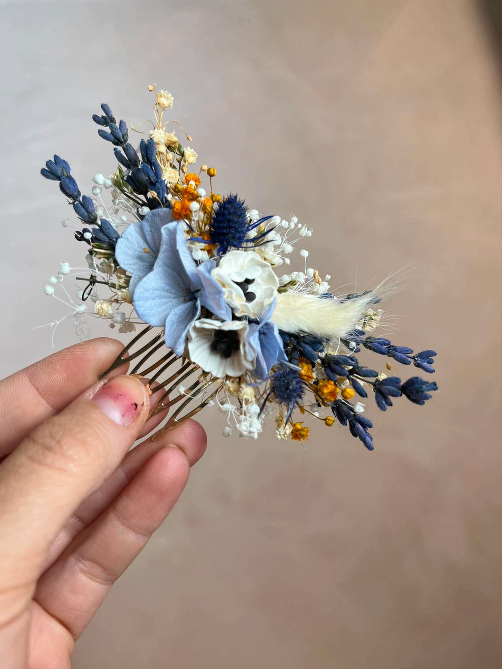 Dusty blue hair comb with  textile anemones in white, preserved powder blue hydrangea, lavender, navy thistles, gypsophila, and warm ochre dried florals, all nestled into a lush, textured arrangement that feels effortlessly natural and deeply romantic