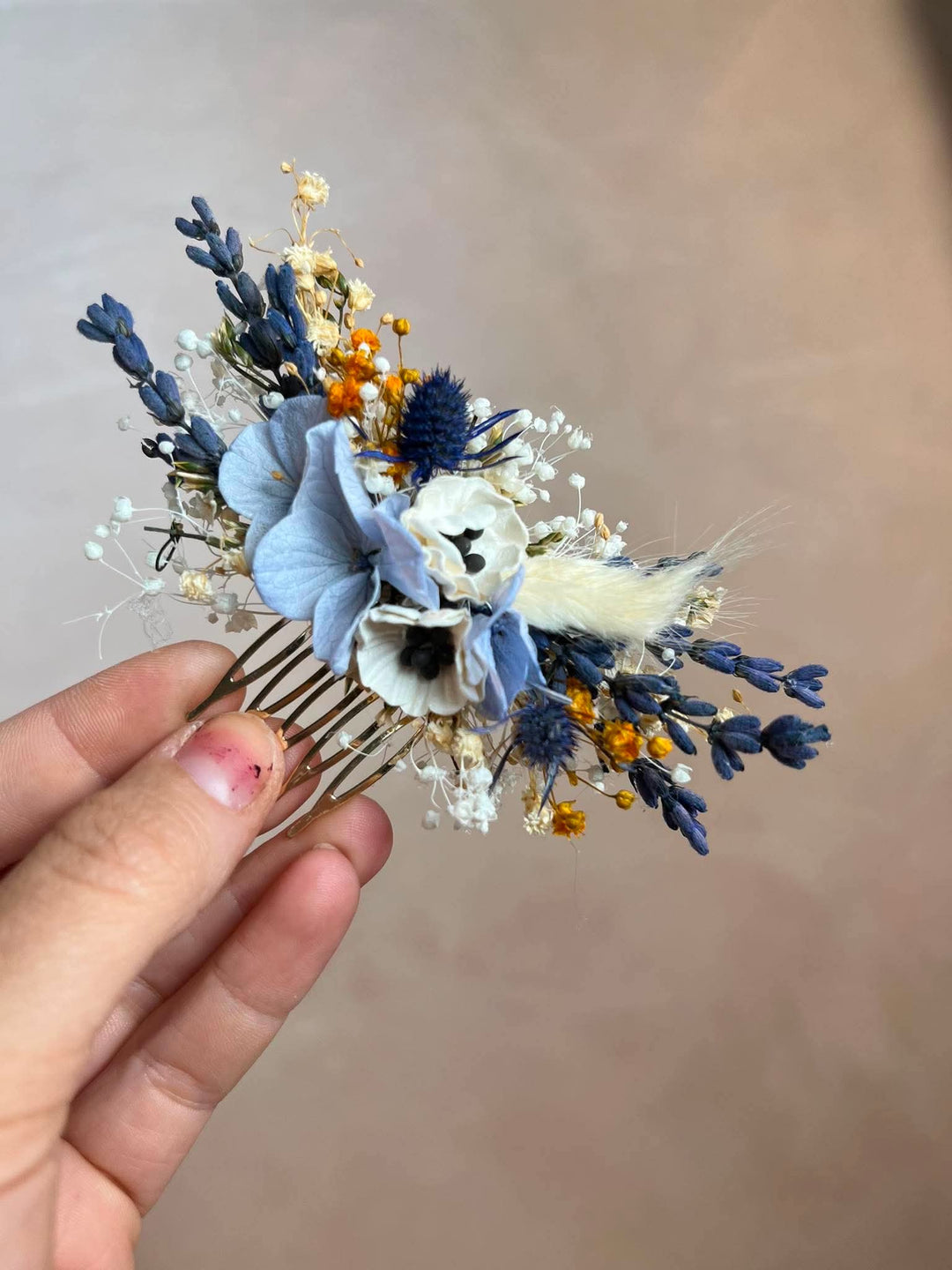 Dusty blue hair comb with  textile anemones in white, preserved powder blue hydrangea, lavender, navy thistles, gypsophila, and warm ochre dried florals, all nestled into a lush, textured arrangement that feels effortlessly natural and deeply romantic
