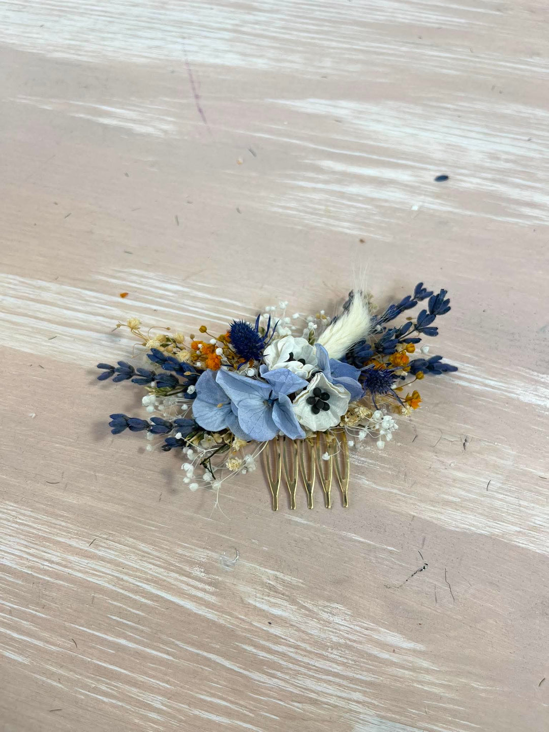 Dusty blue hair comb with  textile anemones in white, preserved powder blue hydrangea, lavender, navy thistles, gypsophila, and warm ochre dried florals, all nestled into a lush, textured arrangement that feels effortlessly natural and deeply romantic