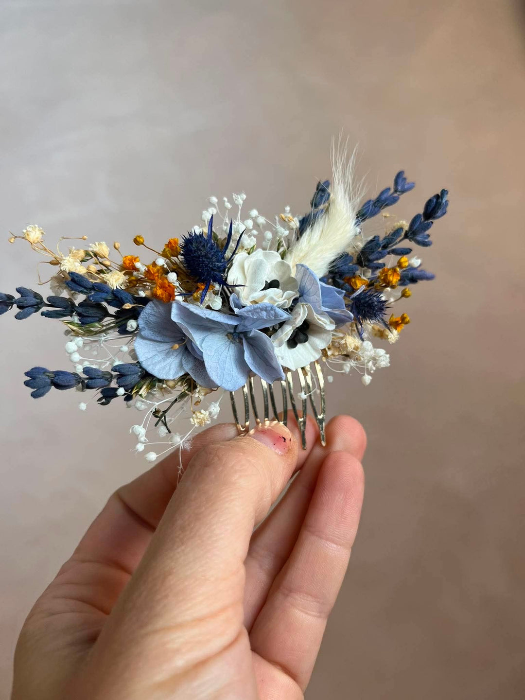 Dusty blue hair comb with  textile anemones in white, preserved powder blue hydrangea, lavender, navy thistles, gypsophila, and warm ochre dried florals, all nestled into a lush, textured arrangement that feels effortlessly natural and deeply romantic