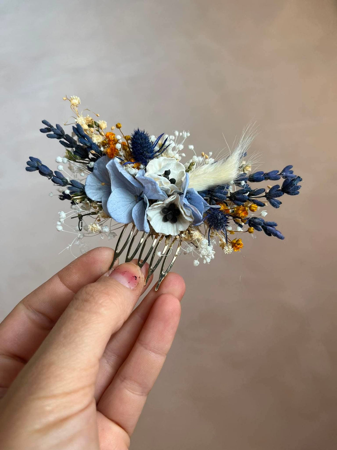 Dusty blue hair comb with  textile anemones in white, preserved powder blue hydrangea, lavender, navy thistles, gypsophila, and warm ochre dried florals, all nestled into a lush, textured arrangement that feels effortlessly natural and deeply romantic