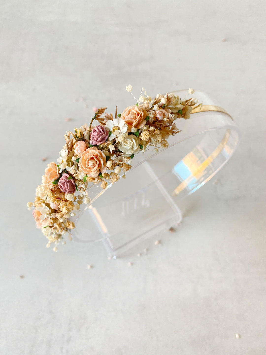 A clear acrylic bangle head decorated with pastel flowers in pink, peach, cream, and gold-toned accents, displayed on a clear stand against a light neutral background.