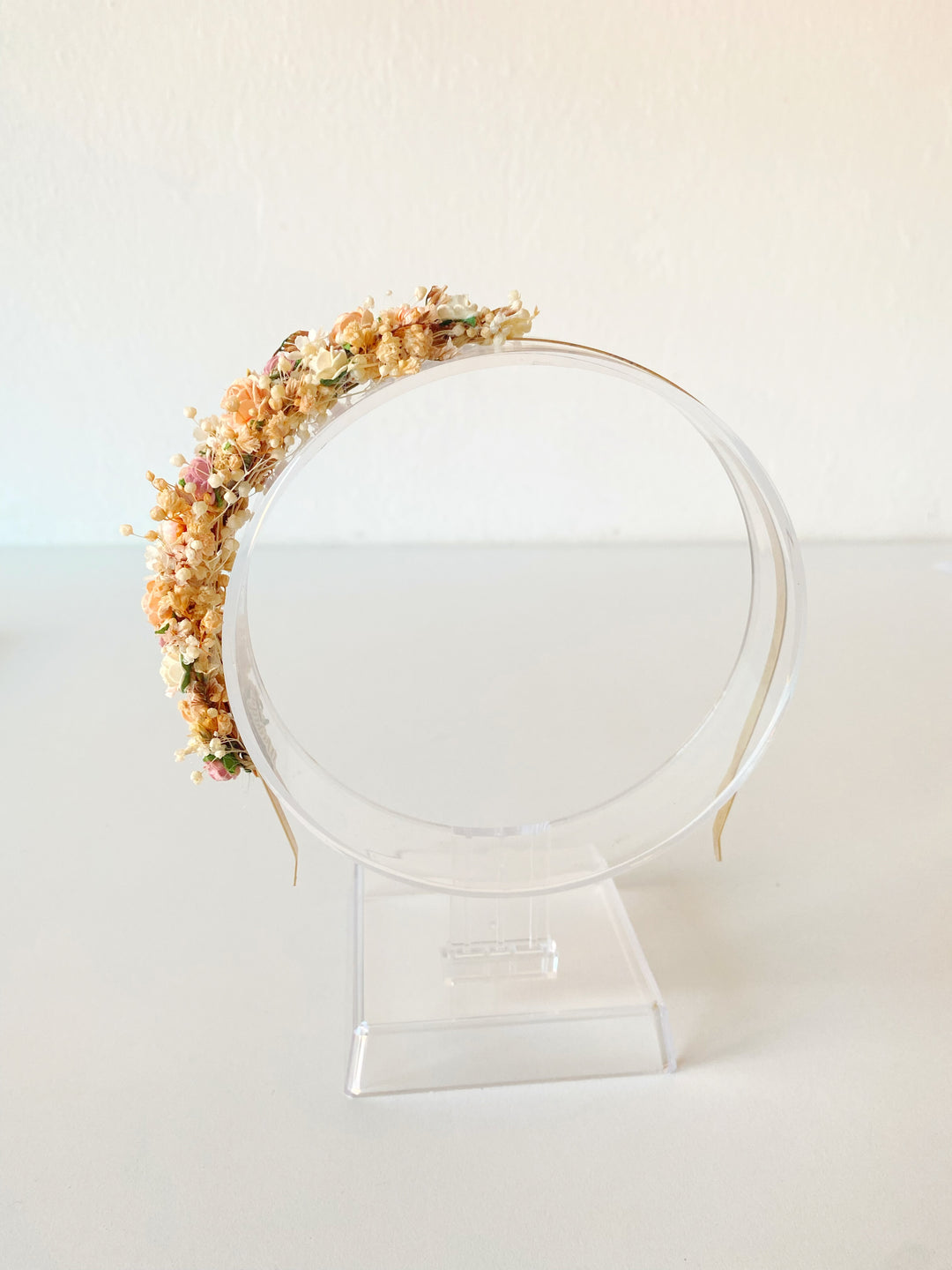 A floral headband with pastel flowers, displayed on a clear acrylic stand against a plain off-white background.