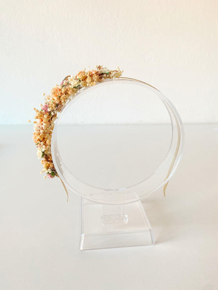 A floral headband with pastel flowers, displayed on a clear acrylic stand against a plain off-white background.