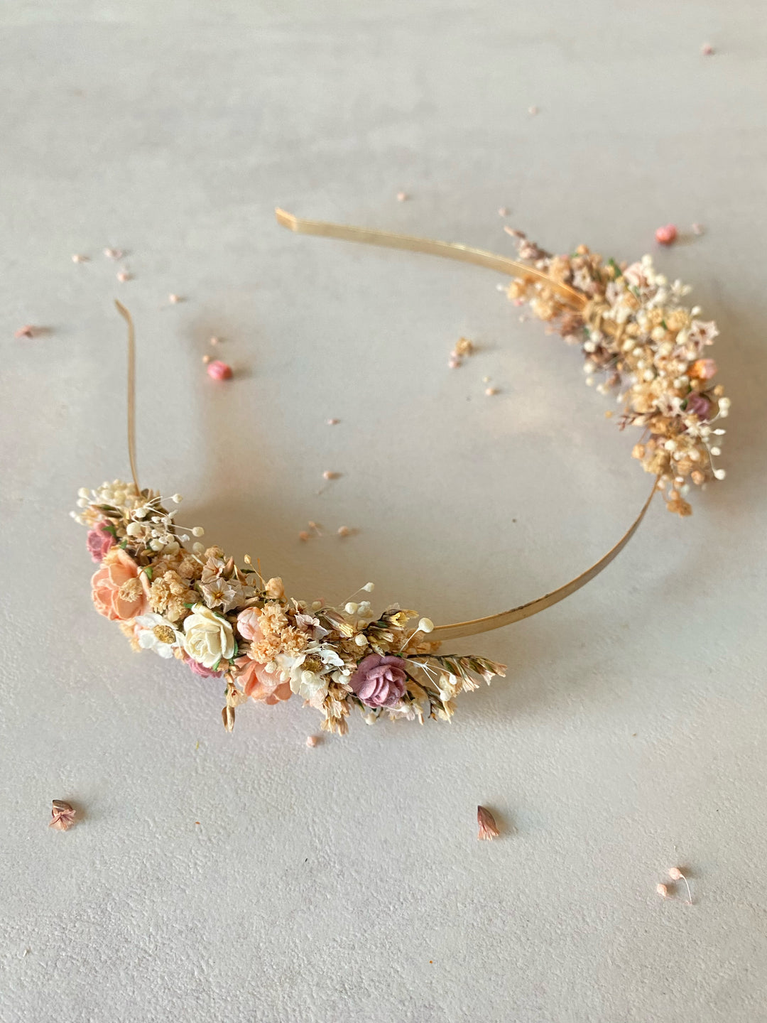 A delicate floral headband with flowers and baby's breath, displayed on a neutral textured background.