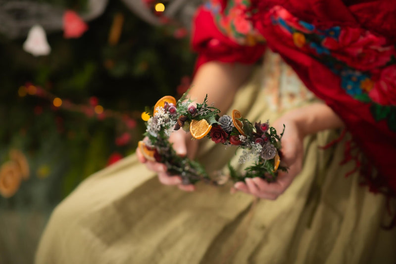 Person holding a floral wreath with oranges against a blurred festive background