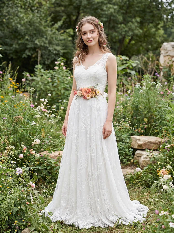 Woman in a white wedding dress standing in a garden with flower blush belt and greenery.