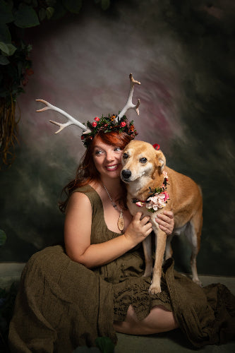 Woman with antlers and a dog in a forest setting