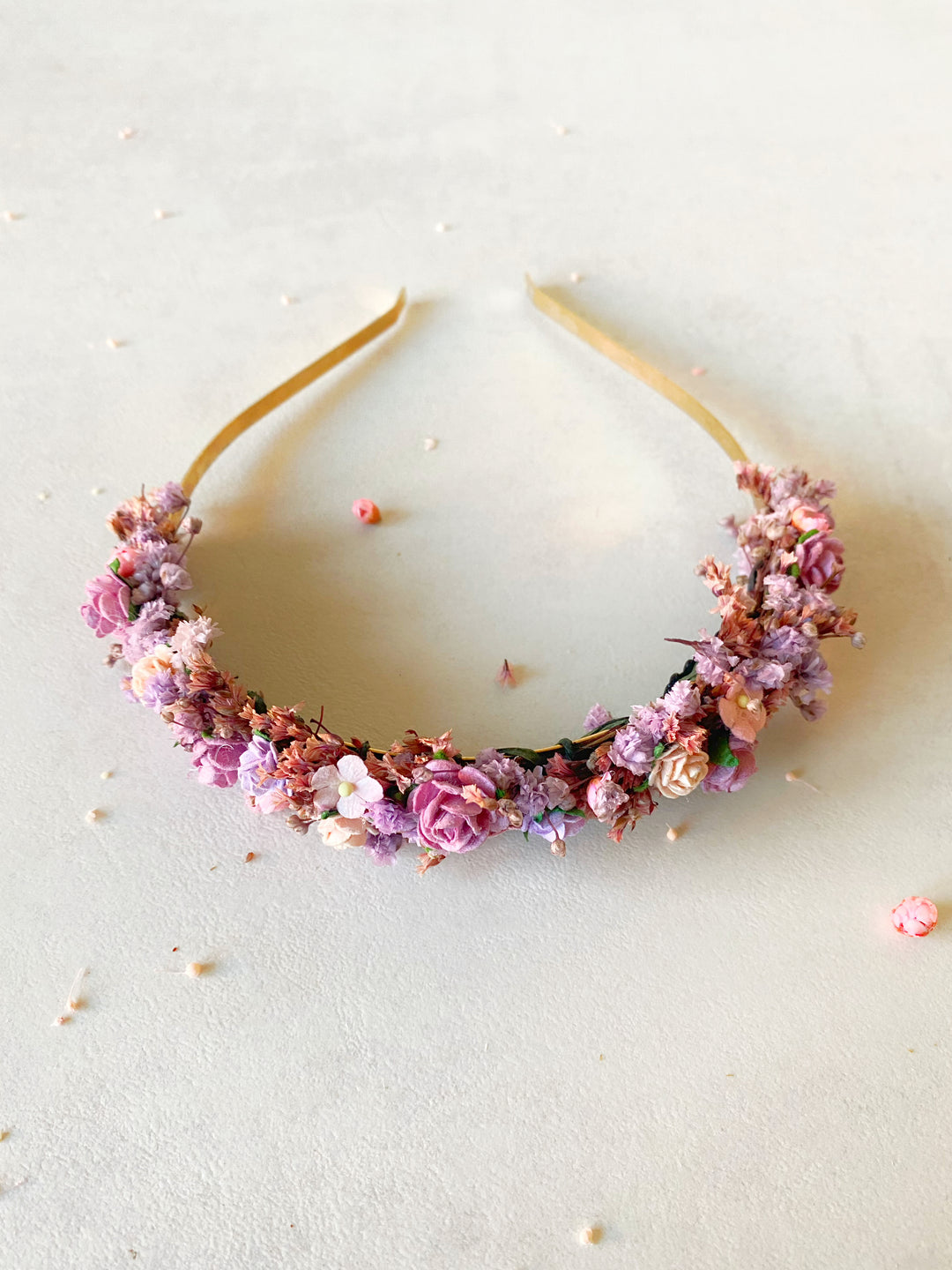A floral headband with pink, purple, and peach flowers on a light beige background.