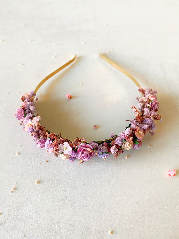 A floral headband with pink, purple, and peach flowers on a light beige background.