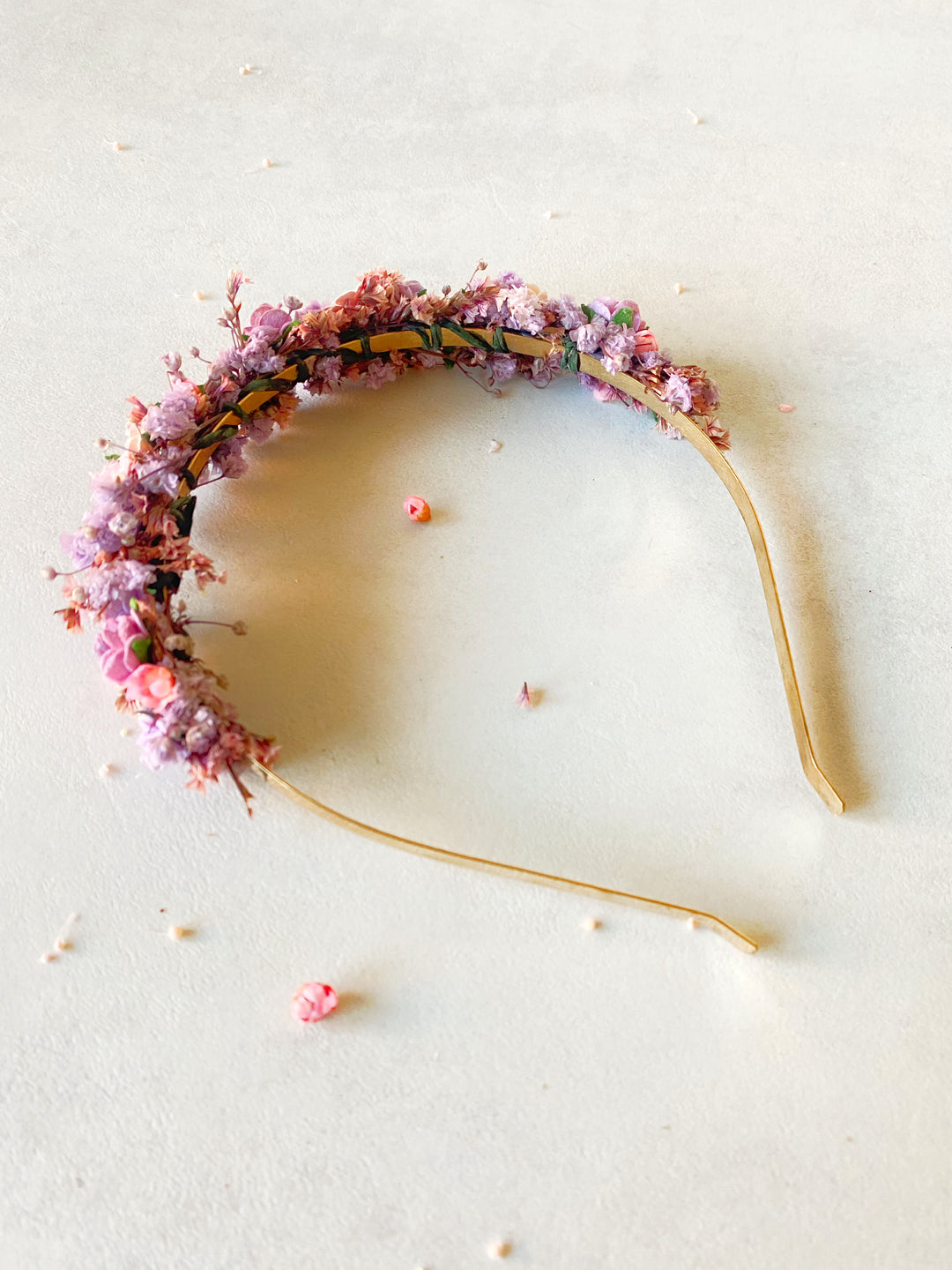 A floral headband decorated with small pink and purple flowers, laid flat on a light beige textured surface.