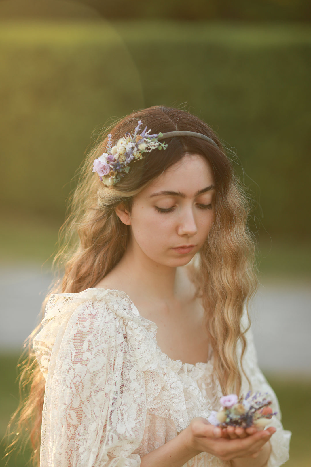 Woman in a white lace dress holding flowers with a blurred green background