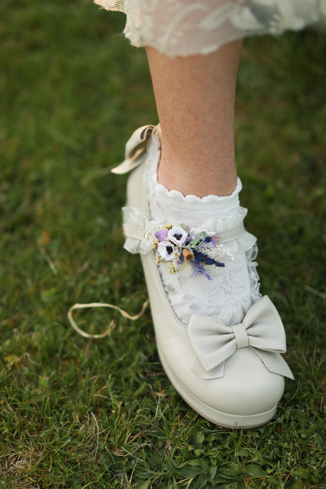 White lace-up shoes with floral embellishments on a grassy background