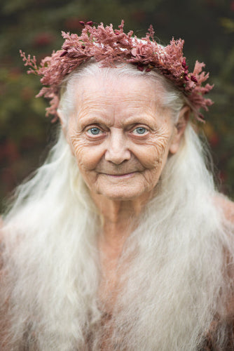 Woman with long white hair wearing a floral headpiece against a blurred natural background