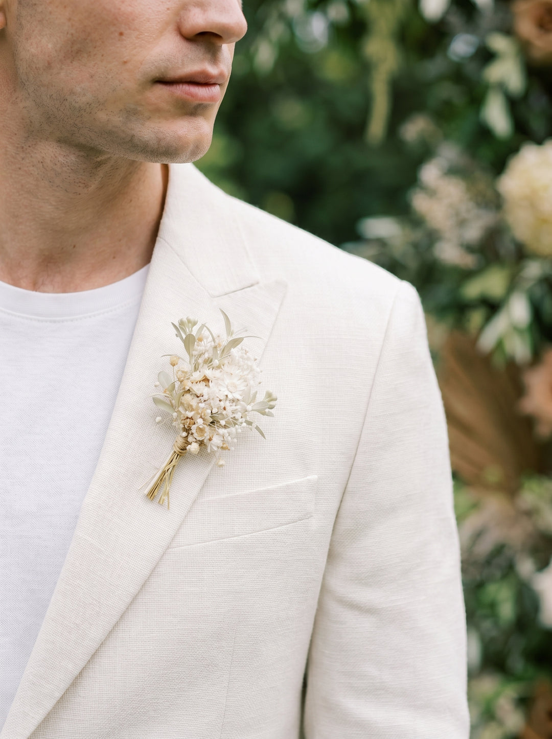 Man wearing a light-colored suit with a floral boutonniere against a blurred natural background