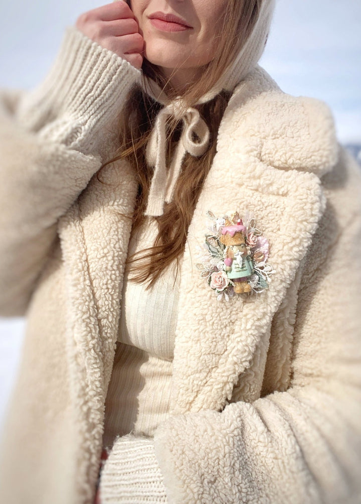 Woman in cream coat with pastel Nutcracker brooch 