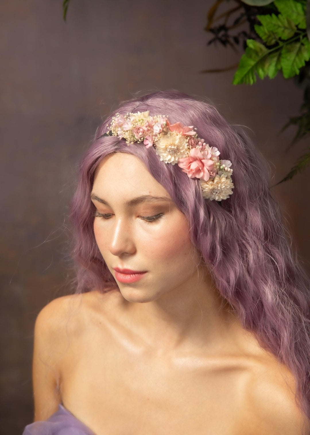 Woman with purple hair wearing a floral headband against a blurred natural background