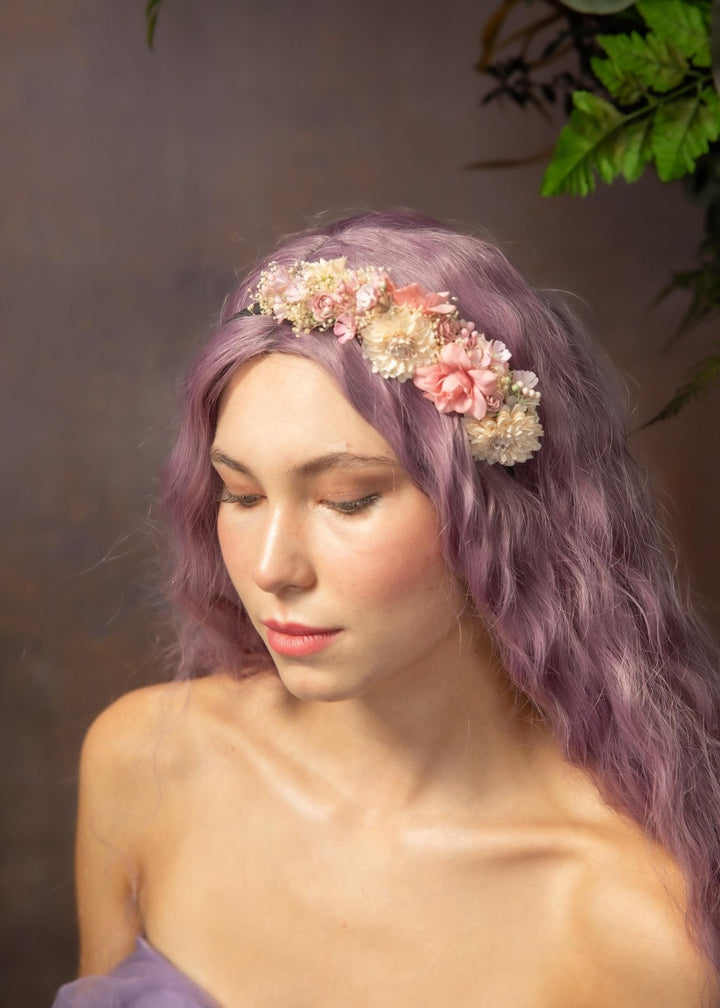 Woman with purple hair wearing a floral headband against a blurred natural background