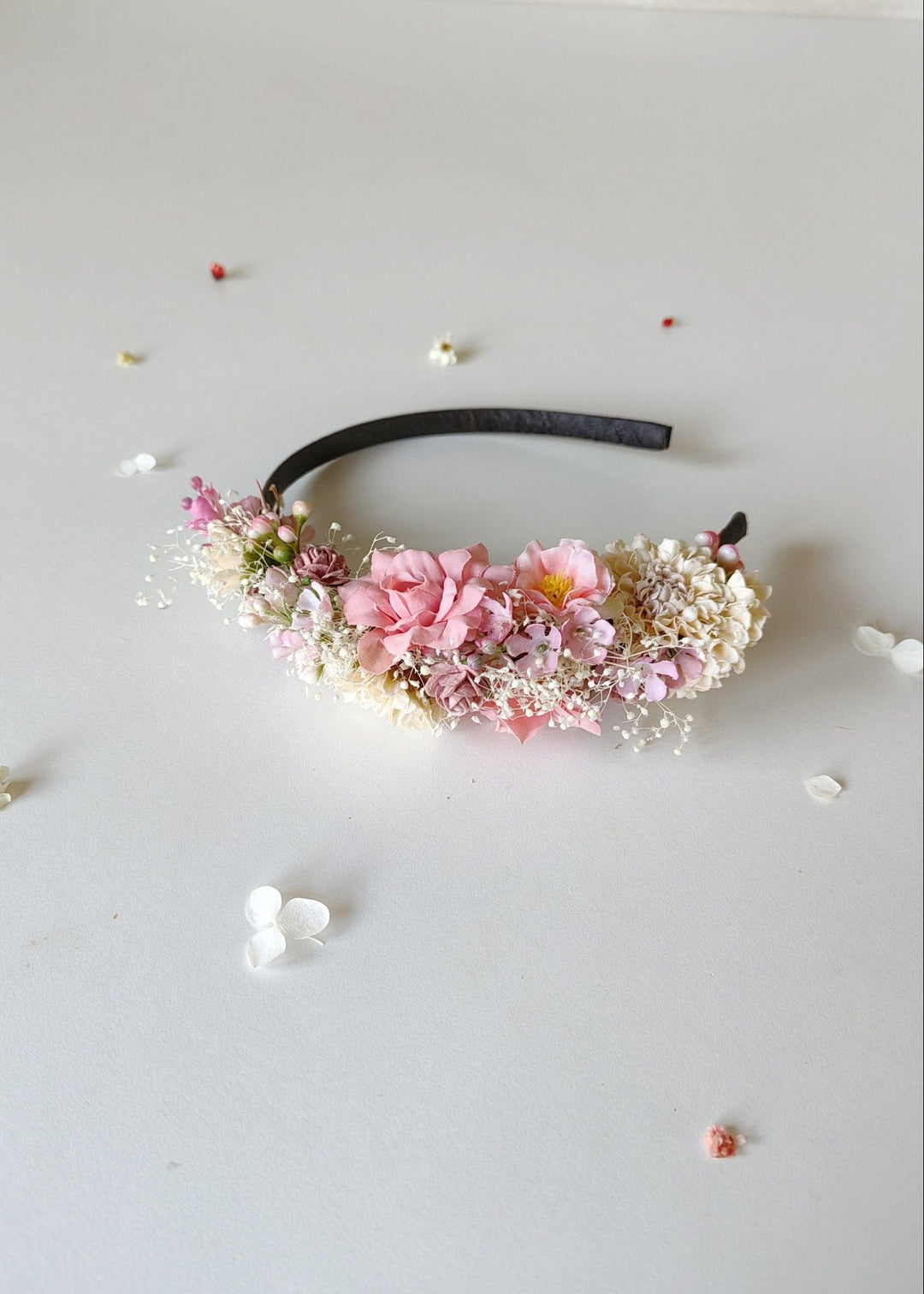 Floral headband with pink flowers and green leaves on a light gray background