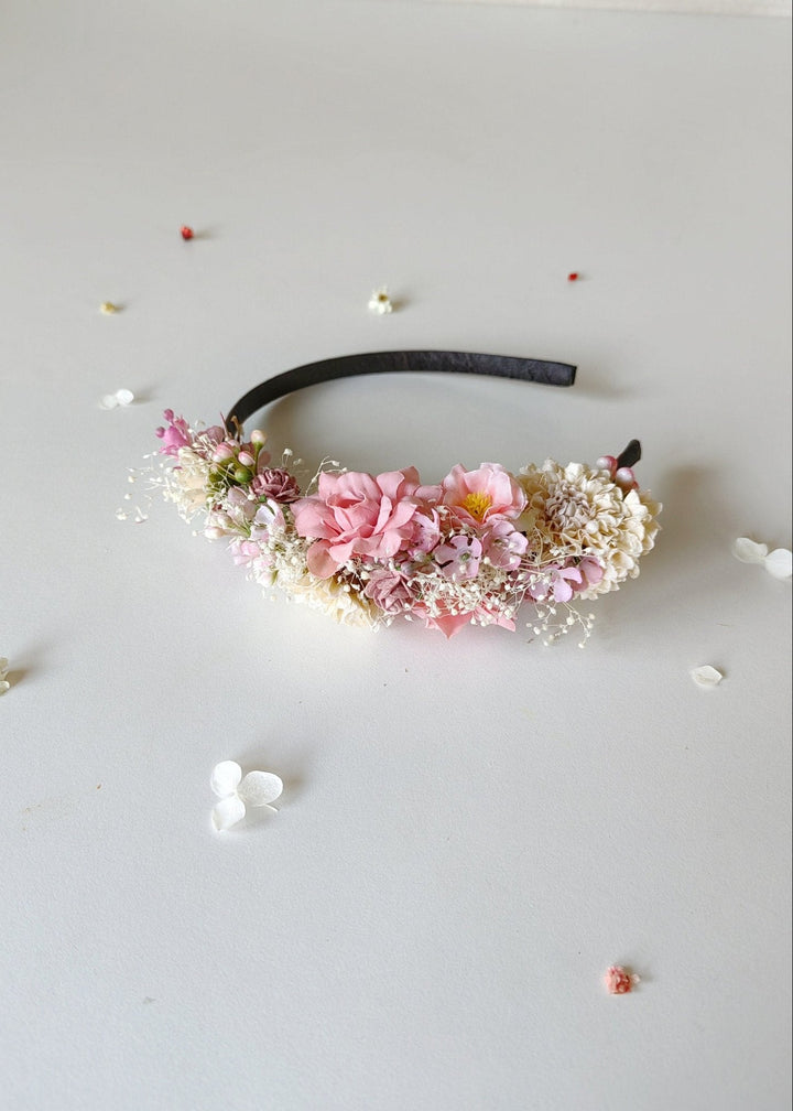 Floral headband with pink flowers and green leaves on a light gray background