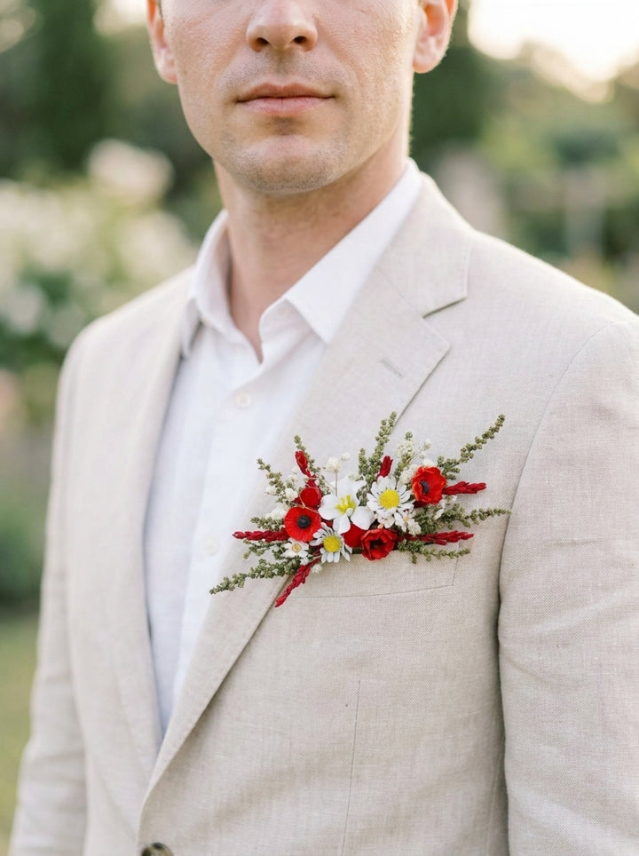 A close-up of a man wearing a light beige linen suit jacket over a white dress shirt, featuring a red and white floral boutonniere on his chest.
