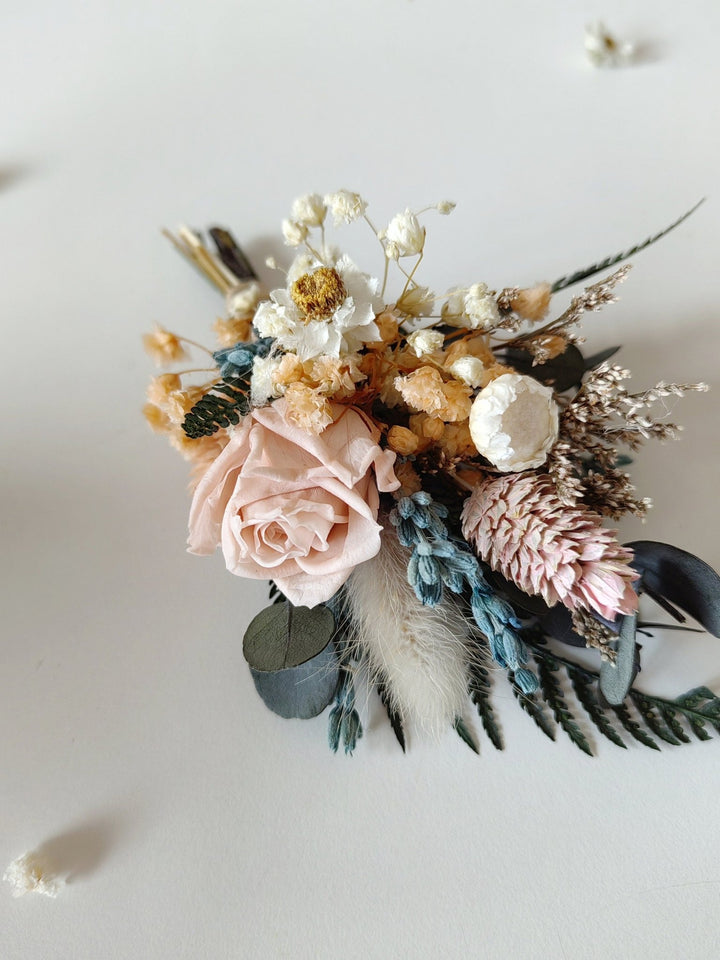 Floral arrangement with pink roses, white flowers, and dried elements on a light background