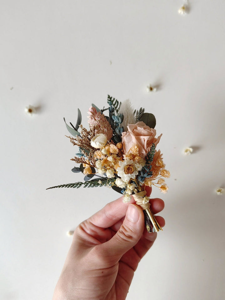 Hand holding a boutonniere for groom of dried flowers against a light background