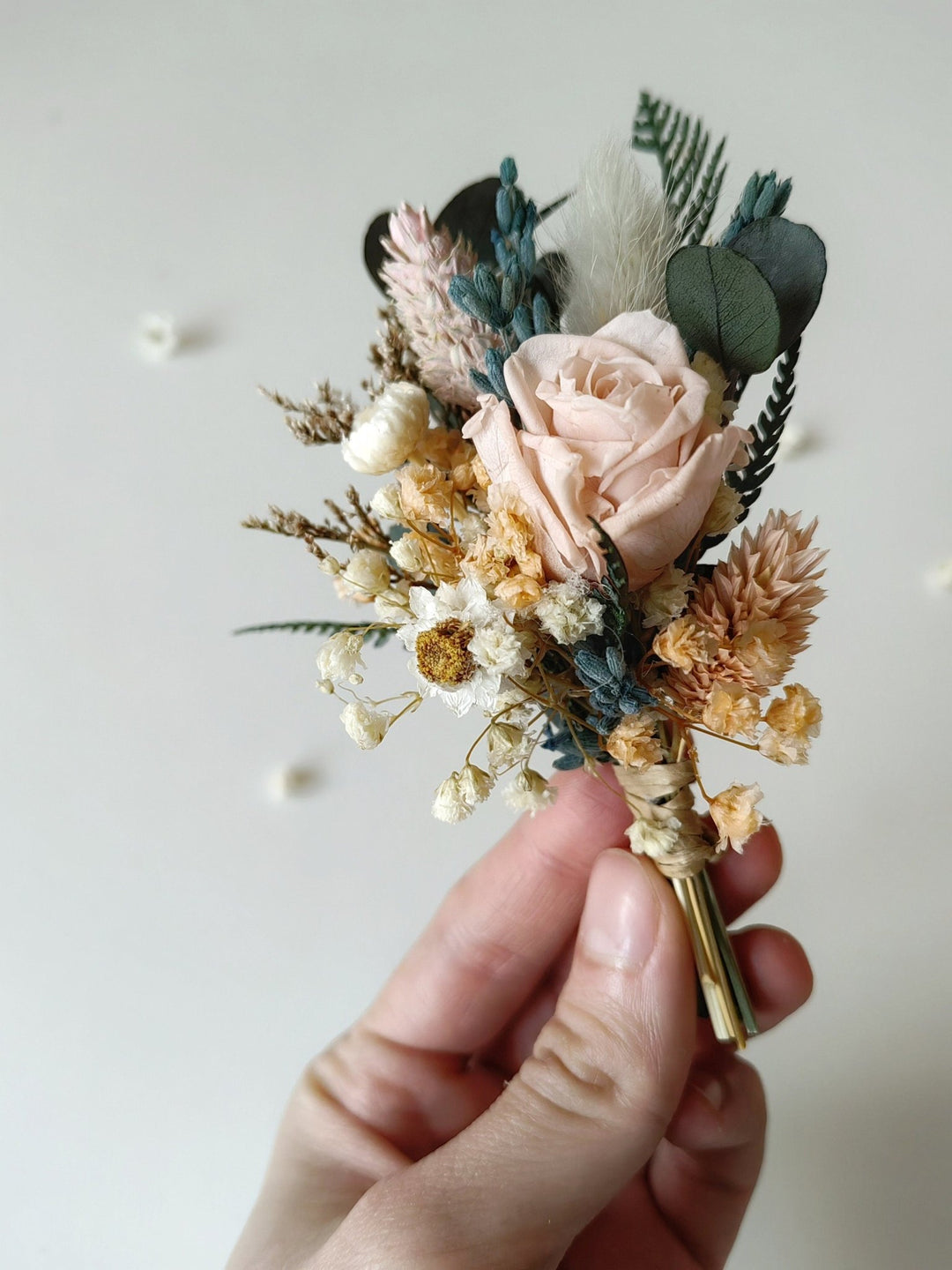 Hand holding a floral boutonniere with a light background