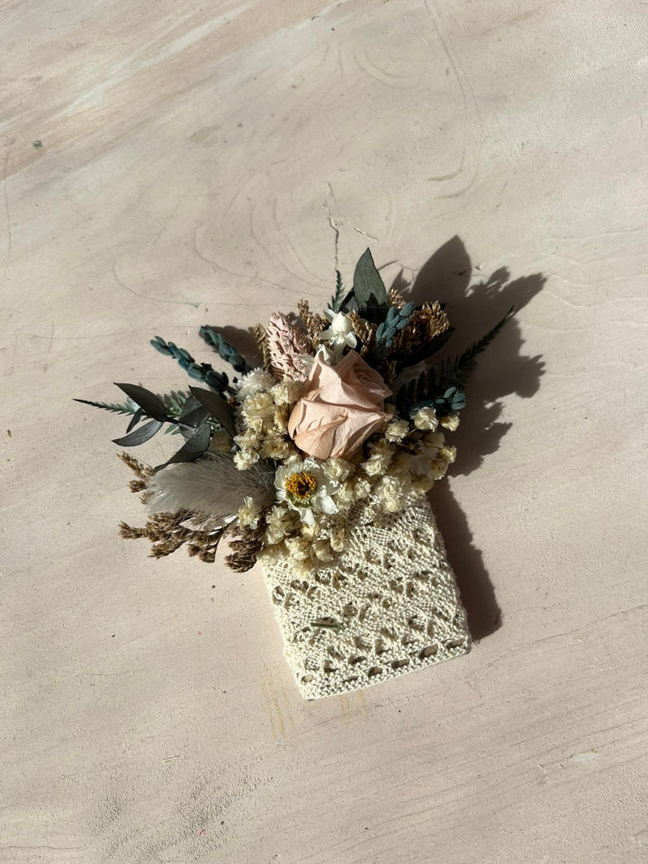 Pocket boutonniere  of dried flowers in a textured vase on a beige surface