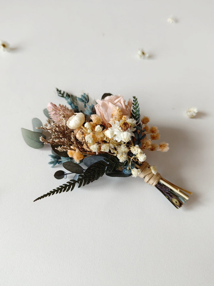 Floral boutonniere with dried flowers and greenery on a light background