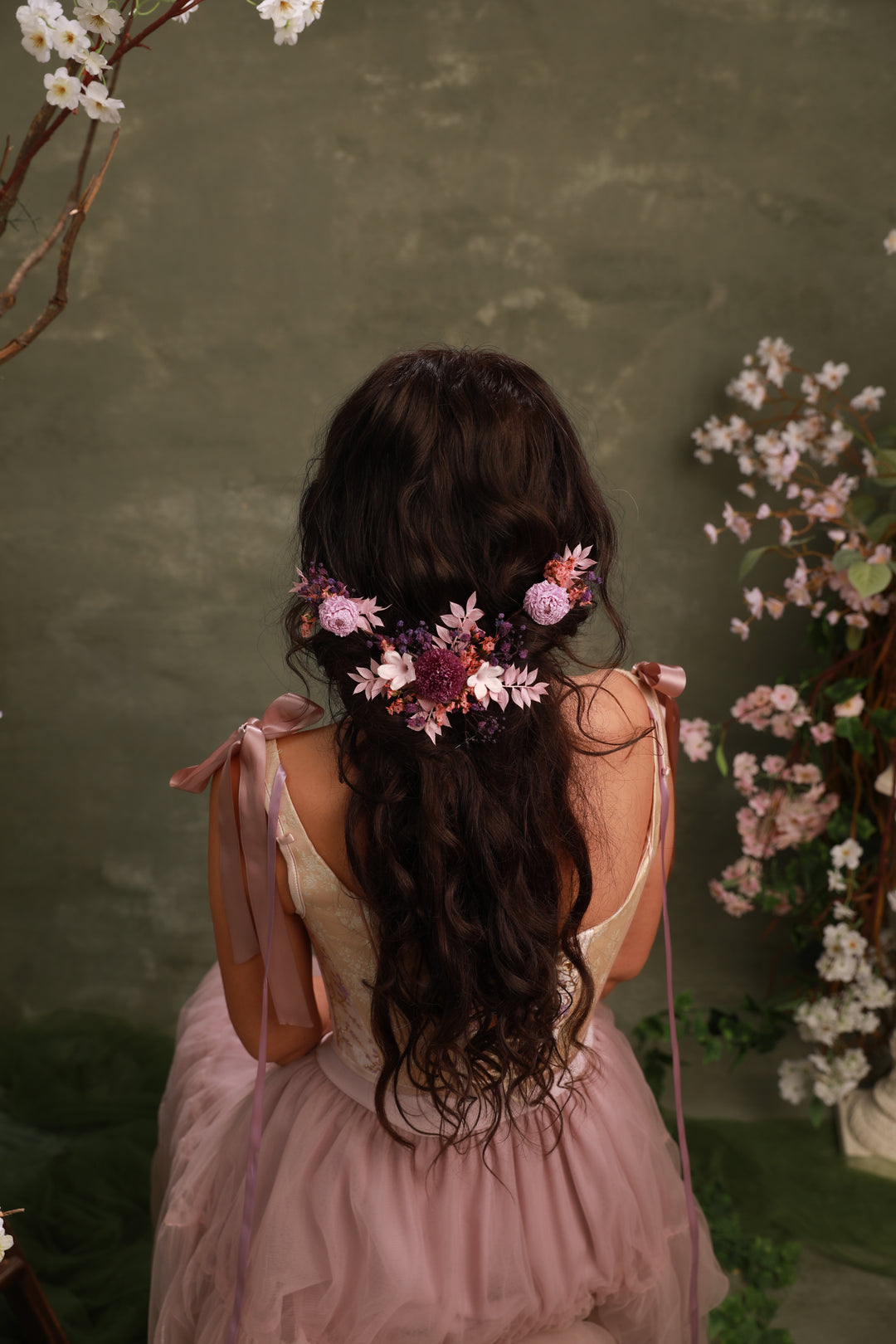 Woman with floral hair accessory in a pink dress against a green background