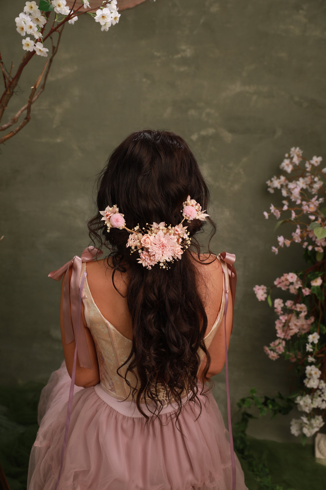 Woman with floral hair accessory from preserved blush flowers and pink dress against a green background