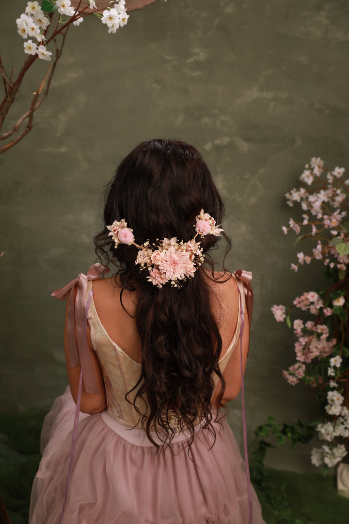 Woman with floral hair accessory from preserved blush flowers and pink dress against a green background