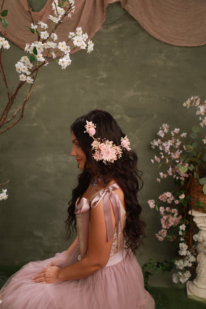 Woman in a pink dress with floral hair accessories against a green wall with floral decorations.